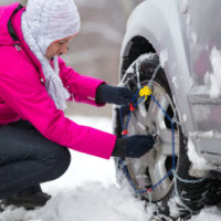 woman putting snow chain on her tires